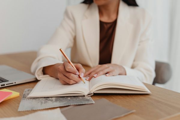 professional woman in white jacket writing in notebook