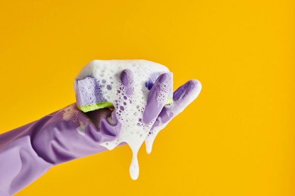 hand wearing purple glove holding sponge yellow background