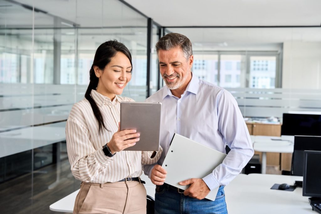 two business professionals standing in a office reviewing information on a tablet about commercial cleaning services